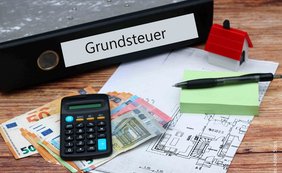 Bundesfinanzhof hält Grundsteuer „Bundesmodell“ für verfassungskonform Ordner mit Aufschrift Grundsteuer, Taschenrechner, Kugelschreiber, Notizblock, Geldscheine, Grundrissplan
